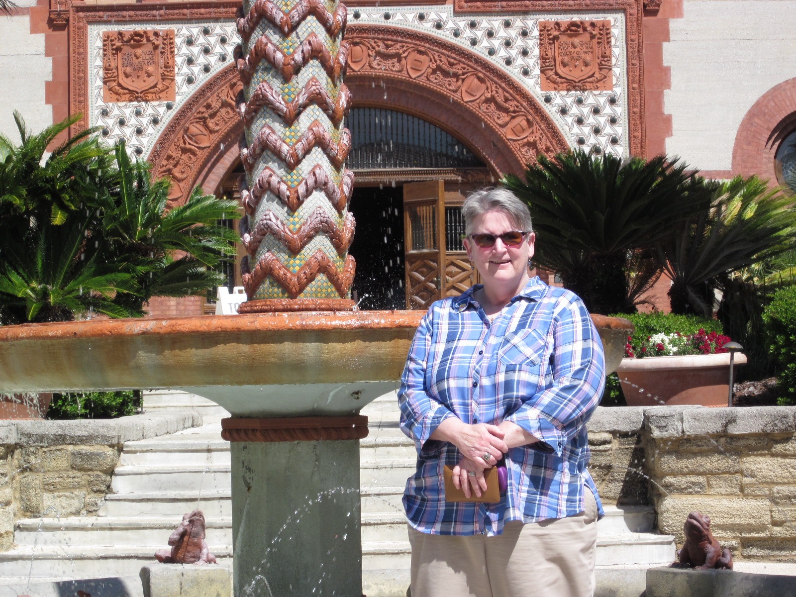 A woman stands gracefully in front of a fountain, water cascading behind her in a serene outdoor setting.