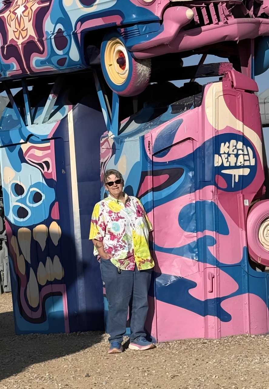 A woman stands beside a vibrant carousel adorned with colorful horses and lights, capturing a joyful amusement park scene.