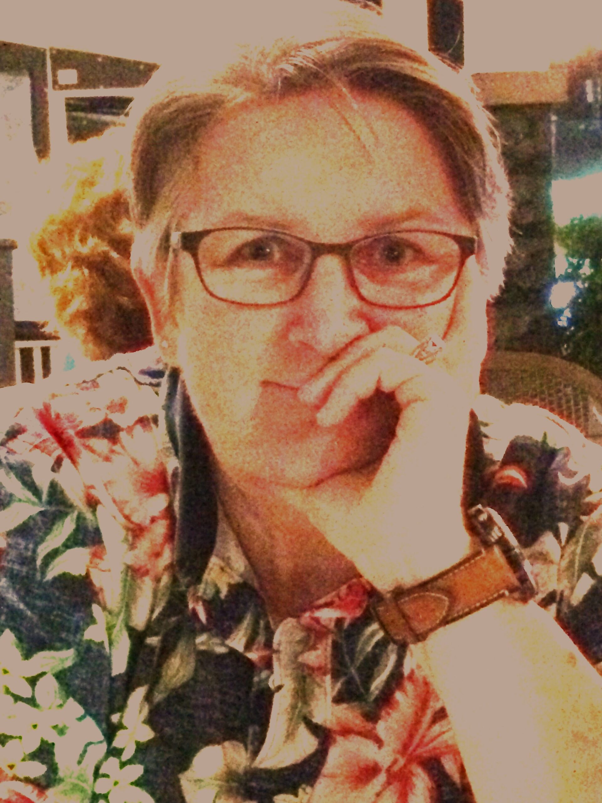 A woman with glasses wearing a colorful floral shirt, smiling and looking towards the camera.